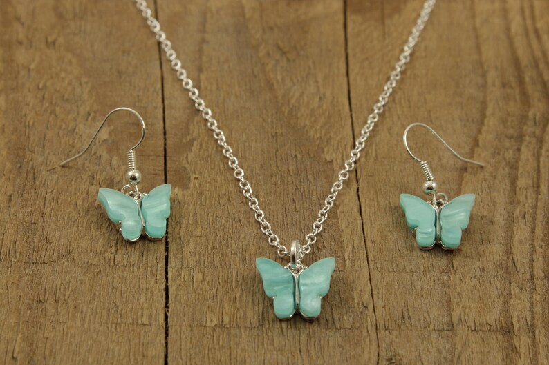 May include: A silver necklace and earrings set with a light blue butterfly pendant and matching earrings.