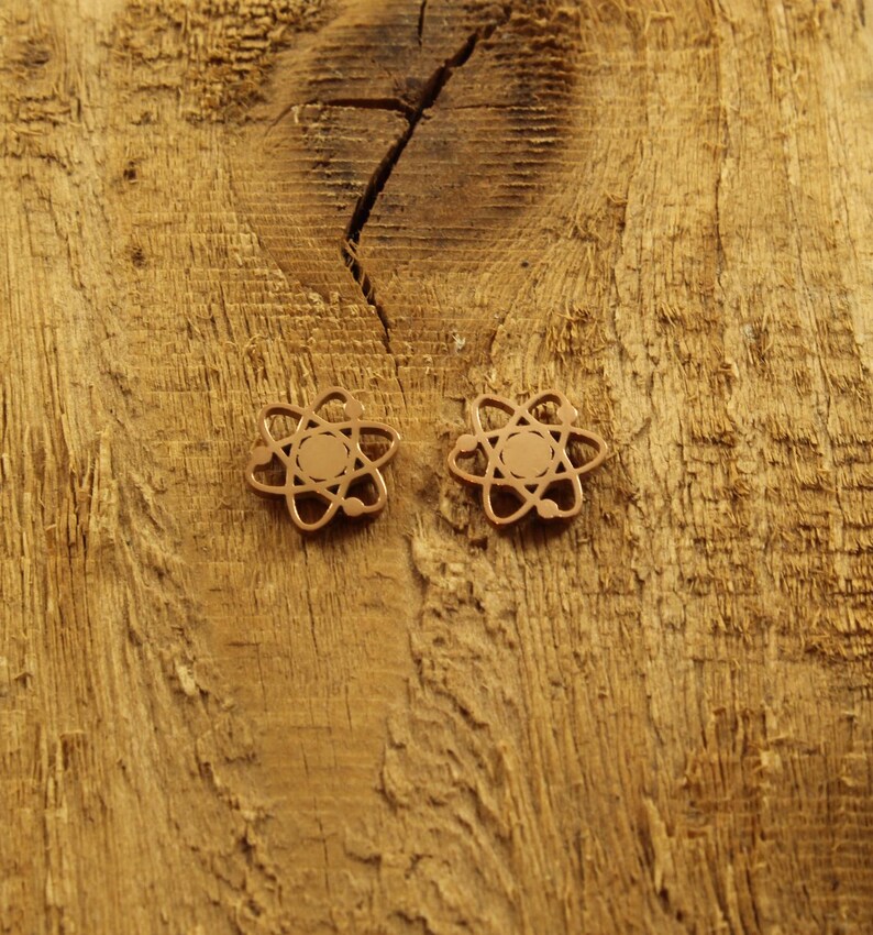 May include: A pair of gold-colored atom earrings on a wooden surface.