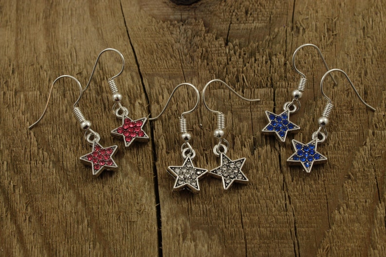 May include: A set of six star-shaped dangle earrings with crystal accents. The earrings are silver-toned and feature red, blue, and clear crystals.
