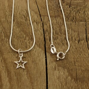 May include: Two silver chains, one with a star-shaped pendant. The chains are on a wooden surface.