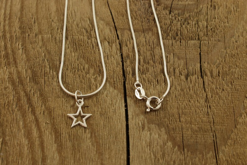 May include: Two silver chains, one with a star-shaped pendant. The chains are on a wooden surface.