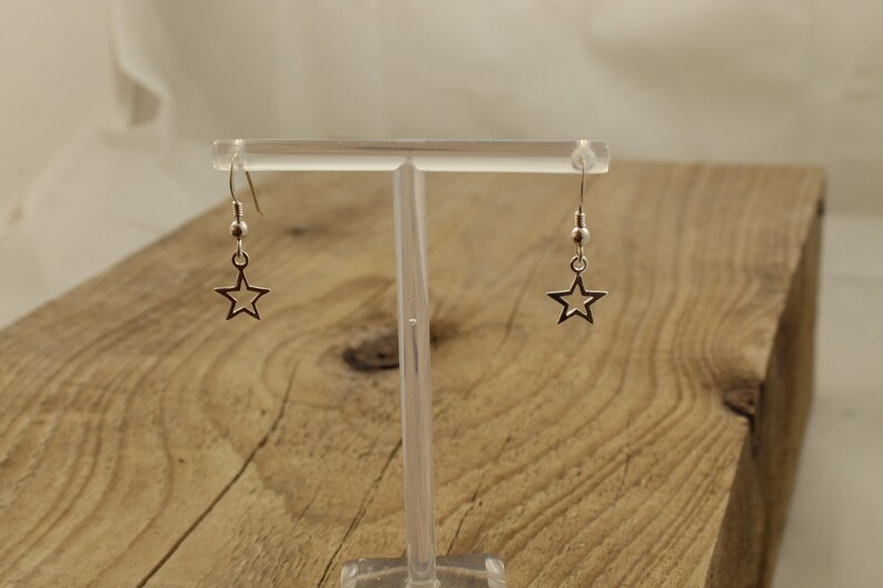 May include: A pair of silver star-shaped dangle earrings with a small bead at the top of each earring.