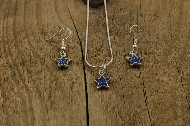May include: A silver necklace and earrings set with a blue star-shaped pendant and matching earrings. The stars are covered in small blue rhinestones.