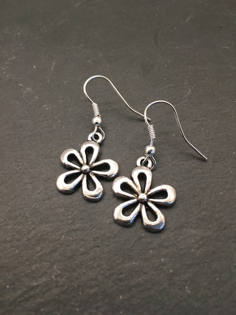 Pu&ograve; includere: Un paio di orecchini pendenti a forma di fiore in argento con un design semplice. Gli orecchini hanno una chiusura a gancio.