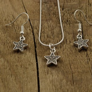 May include: A silver necklace and earrings set with star-shaped pendants encrusted with clear rhinestones.