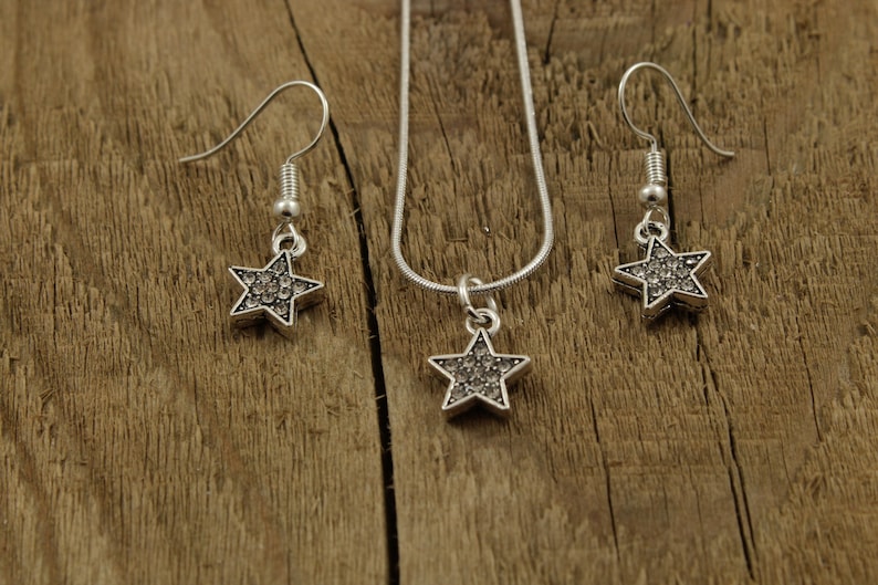 May include: A silver necklace and earrings set with star-shaped pendants encrusted with clear rhinestones.
