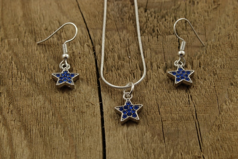 May include: A silver necklace and earrings set with a blue star pendant and matching earrings. The star is covered in small blue rhinestones.