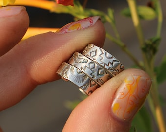 May include: Three silver rings with intricate designs stacked on a finger. The rings are worn by a person with painted fingernails.