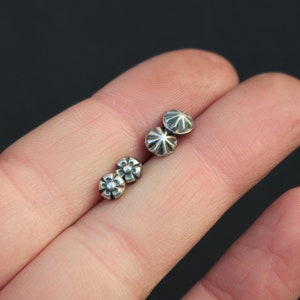 May include: Two pairs of silver stud earrings. One pair features a simple round design, while the other pair has a flower-shaped design.