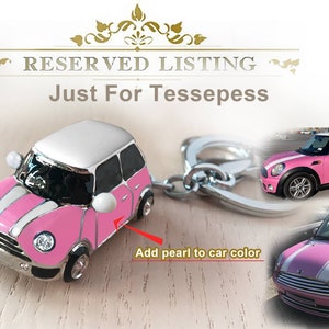May include: A pink and white miniature car keyring with a silver key ring. The car features a white roof and white racing stripes. The image also includes a larger photo of the car.