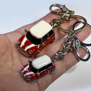 Puede incluir: Dos llaveros en miniatura de coche rojo y blanco con detalles dorados. El llavero m&aacute;s grande est&aacute; unido a una cadena dorada y plateada con un cierre plateado. El llavero m&aacute;s peque&ntilde;o est&aacute; unido al llavero m&aacute;s grande.