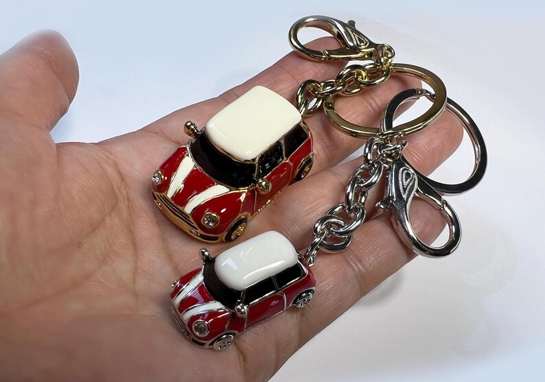 Puede incluir: Dos llaveros en miniatura de coche rojo y blanco con detalles dorados. El llavero m&aacute;s grande est&aacute; unido a una cadena dorada y plateada con un cierre plateado. El llavero m&aacute;s peque&ntilde;o est&aacute; unido al llavero m&aacute;s grande.