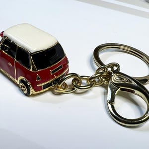 Puede incluir: Un llavero de coche en miniatura rojo y blanco con una cadena dorada y un cierre dorado.