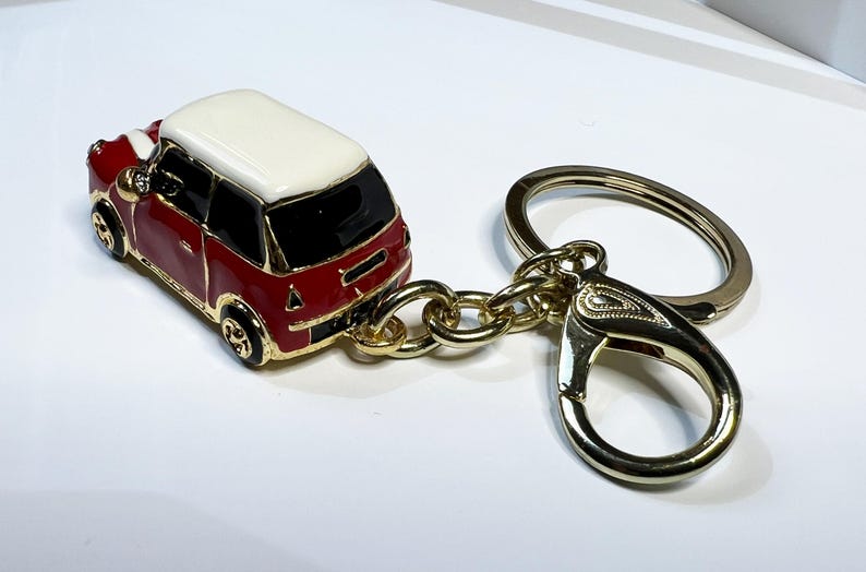 Puede incluir: Un llavero de coche en miniatura rojo y blanco con una cadena dorada y un cierre dorado.