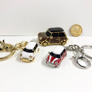 Puede incluir: Tres llaveros de coche en miniatura con anillas doradas y plateadas. Los coches son un mini cooper blanco, uno rojo y uno marr&oacute;n.