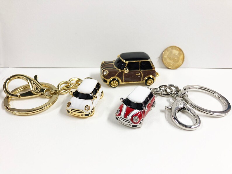 Puede incluir: Tres llaveros de coche en miniatura con anillas doradas y plateadas. Los coches son un mini cooper blanco, uno rojo y uno marr&oacute;n.
