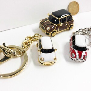 Puede incluir: Tres llaveros de coche en miniatura. Uno es marr&oacute;n con ribetes negros, otro es blanco con ribetes negros y otro es rojo y blanco con ribetes negros. Los tres llaveros tienen anillos dorados.