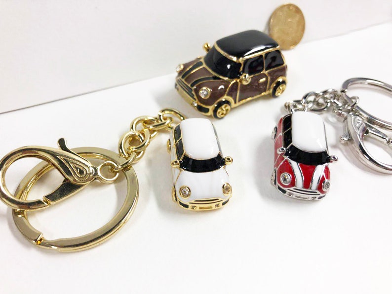 Puede incluir: Tres llaveros de coche en miniatura. Uno es marr&oacute;n con ribetes negros, otro es blanco con ribetes negros y otro es rojo y blanco con ribetes negros. Los tres llaveros tienen anillos dorados.