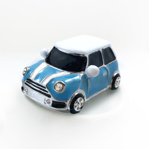May include: A small, blue and white car with black detailing and a white roof. The car features a silver grille with the letters "K&L" and a decorative jewel in the headlights.