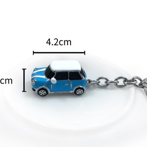 May include: A blue and white miniature car keyring, measuring 4.2 cm long and 2.5 cm high. The car has a silver chain and key ring. The keyring is a miniature replica of a classic car.