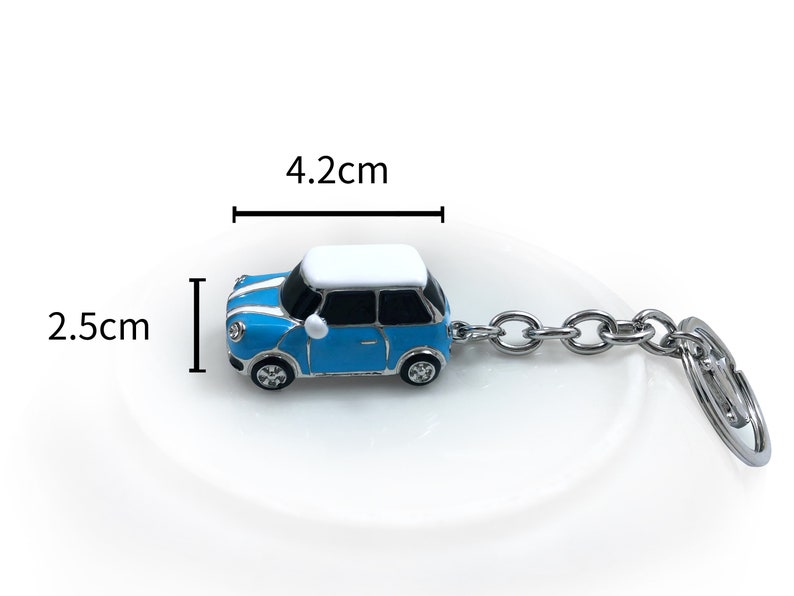 May include: A blue and white miniature car keyring, measuring 4.2 cm long and 2.5 cm high. The car has a silver chain and key ring. The keyring is a miniature replica of a classic car.