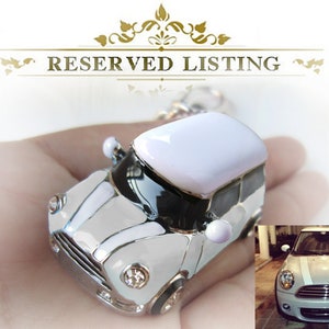 May include: A miniature white and silver car keyring with a white roof and black detailing. The keyring features a detailed design and a small image of a car in the bottom right. The text "RESERVED LISTING" is at the top.