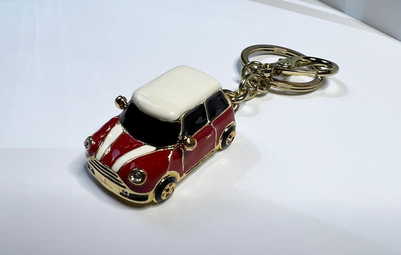 Puede incluir: Un llavero de coche Mini Cooper rojo y blanco con un anillo de llave de metal dorado.