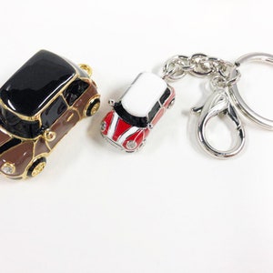Puede incluir: Dos llaveros de coche en miniatura. Uno es marr&oacute;n y negro con detalles dorados. El otro es rojo, blanco y negro con un llavero plateado.