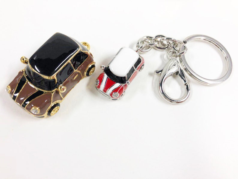 Puede incluir: Dos llaveros de coche en miniatura. Uno es marr&oacute;n y negro con detalles dorados. El otro es rojo, blanco y negro con un llavero plateado.