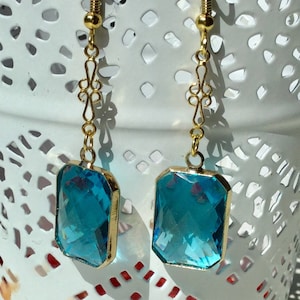 May include: A pair of gold dangle earrings with a blue gemstone. The earrings have a delicate, ornate design and feature a rectangular blue gemstone.