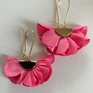 May include: A pair of pink flower-shaped earrings with gold-toned metal hoops and a half-circle accent.