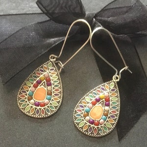 May include: A pair of silver teardrop earrings with colourful enamel and bead accents. The earrings have a teardrop shape with a silver hook.