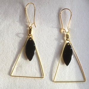 May include: A pair of gold triangle earrings with black teardrop-shaped charms hanging from the bottom.