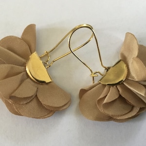 Peut inclure: Une paire de boucles d'oreilles dorées avec un motif de fleur en tissu beige.