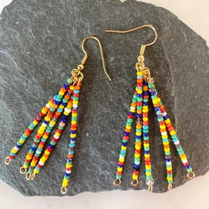 May include: A pair of colourful beaded dangle earrings with gold hooks. The beads are arranged in a cascading pattern of red, orange, yellow, green, blue, and purple.