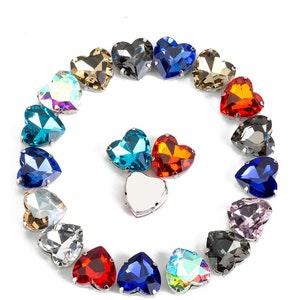 Könnte beinhalten: Sortiment an herzförmigen Strasssteinen in verschiedenen Farben, darunter Rot, Blau, Grün, Klar und Irisierend. Die Strasssteine sind in einem Kreis auf weißem Hintergrund angeordnet.