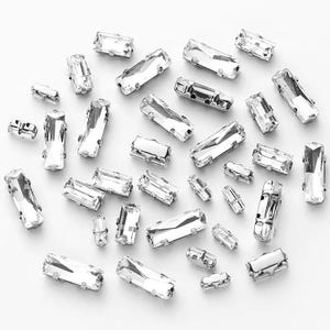 Peut inclure: Un ensemble de perles de cristal rectangulaires transparentes dispersées sur une surface blanche. Les perles varient en taille et présentent un design à facettes, reflétant la lumière. Idéal pour la création de bijoux ou les projets d'artisanat.