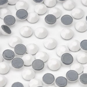 Könnte beinhalten: Nahaufnahme von weißen und grauen runden Strasssteinen. Die Strasssteine sind auf einer weißen Oberfläche verstreut.