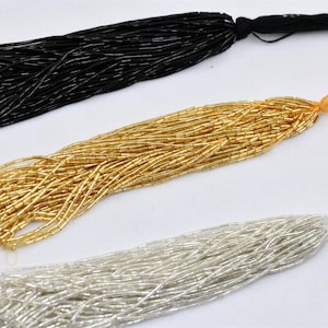 Pode incluir: Três fios de contas de vidro, um preto, um dourado e um prateado. Cada fio tem uma borla na ponta.