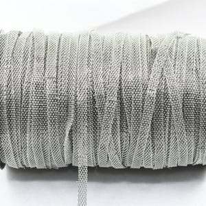 May include: A spool of silver mesh ribbon. The ribbon is tightly wound on a black plastic spool. The mesh has a woven appearance, and a small length of ribbon extends from the spool.