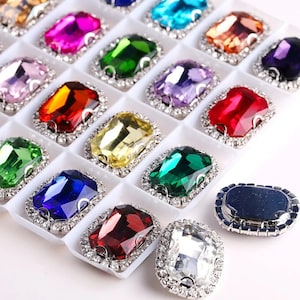 Può includere: Assortimento di strass rettangolari sfaccettati di colori vivaci con montature argentate. Gli strass sono disposti in una griglia in una teca bianca.