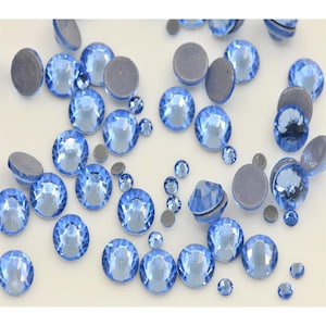 May include: A scattering of light blue rhinestones on a white surface. The rhinestones are various sizes and have a faceted design.