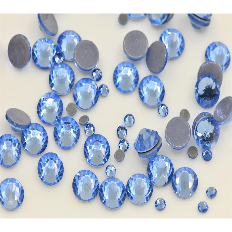May include: A scattering of light blue rhinestones on a white surface. The rhinestones are various sizes and have a faceted design.