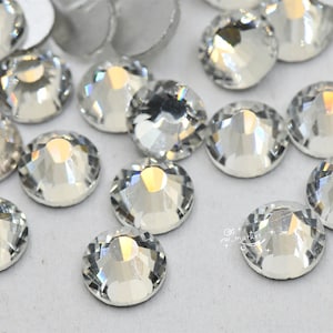 Puede incluir: Primer plano de un grupo de piedras de cristal redondas transparentes. Las piedras de cristal están esparcidas sobre una superficie blanca.