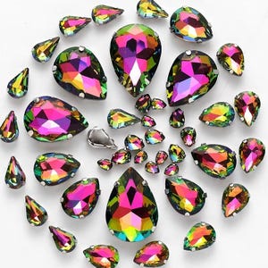 May include: Assortment of iridescent teardrop-shaped rhinestones in various sizes. The rhinestones have a rainbow effect with shades of pink, green, and blue.