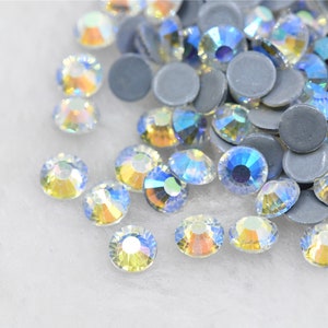 Puede incluir: Un montón de piedras de cristal transparente iridiscente con un efecto arcoíris. Las piedras están esparcidas sobre una superficie blanca.
