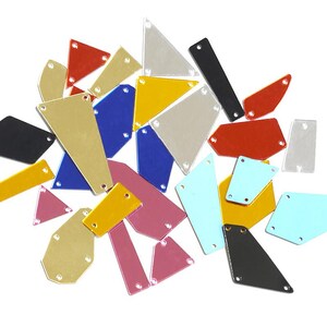 Peut inclure: Un assortiment de strass géométriques multicolores, comprenant des formes triangulaires et rectangulaires. Les strass, de couleurs rouge, bleu et jaune, sont percés de trous et disposés sur un fond blanc.