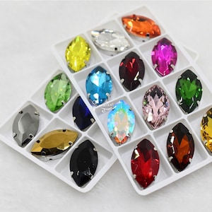 May include: Assortment of 12 marquise-shaped rhinestones in a clear plastic storage case. The rhinestones are in various colours, including red, blue, green, yellow, orange, pink, and black.