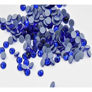 May include: A large quantity of blue rhinestones with adhesive backing. The rhinestones are scattered on a white surface.