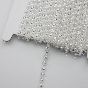 Peut inclure: Rouleau de garniture en strass transparent, avec une ligne continue de strass ronds et étincelants. La garniture est sur un support en carton blanc, idéale pour l'artisanat et les embellissements. Les strass sont clairs et réfléchissants.